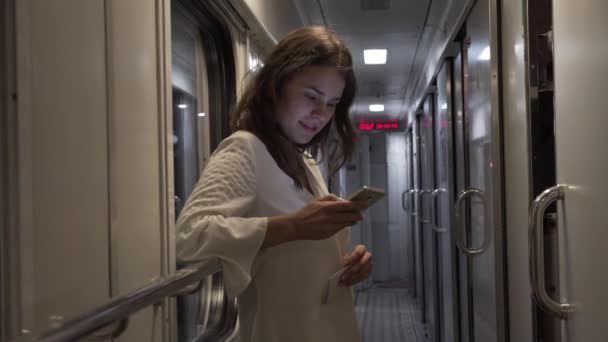 El tema del transporte terrestre y los viajes. Hermosa joven mujer caucásica en la estación de tren esperando la salida del tren dentro del interior del coche. Utiliza tecnología de telefonía móvil — Vídeos de Stock