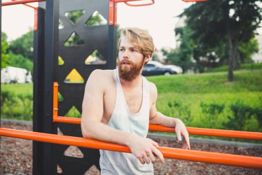 Portre genç sakallı adam kamu spor zemin üzerinde duran ve paralel barlar üzerinde eğitim. Yakışıklı egzersiz atleti. Sakallı portre sportif adam, eğitimden sonra dinlenme. Yaz egzersiz açık havada