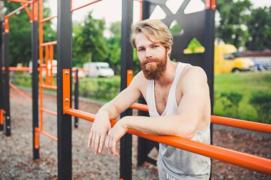 Portre genç sakallı adam kamu spor zemin üzerinde duran ve paralel barlar üzerinde eğitim. Yakışıklı egzersiz atleti. Sakallı portre sportif adam, eğitimden sonra dinlenme. Yaz egzersiz açık havada