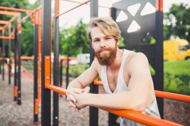 Portre genç sakallı adam kamu spor zemin üzerinde duran ve paralel barlar üzerinde eğitim. Yakışıklı egzersiz atleti. Sakallı portre sportif adam, eğitimden sonra dinlenme. Yaz egzersiz açık havada