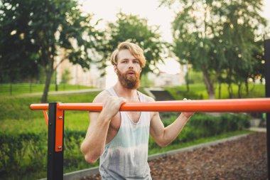 Portre genç sakallı adam kamu spor zemin üzerinde duran ve paralel barlar üzerinde eğitim. Yakışıklı egzersiz atleti. Sakallı portre sportif adam, eğitimden sonra dinlenme. Yaz egzersiz açık havada