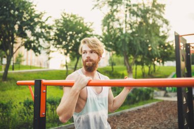 Portre genç sakallı adam kamu spor zemin üzerinde duran ve paralel barlar üzerinde eğitim. Yakışıklı egzersiz atleti. Sakallı portre sportif adam, eğitimden sonra dinlenme. Yaz egzersiz açık havada