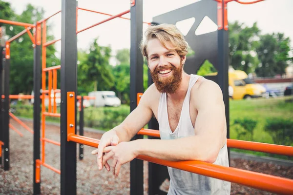 Portrait young bearded man standing on public sports ground and training on parallel bars. Handsome workout athlete. Portrait sporty man with beard, rest after training. Summer workout outdoors — Stock Photo, Image