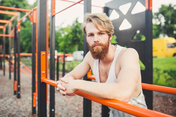 Portrait young bearded man standing on public sports ground and training on parallel bars. Handsome workout athlete. Portrait sporty man with beard, rest after training. Summer workout outdoors — Stock Photo, Image