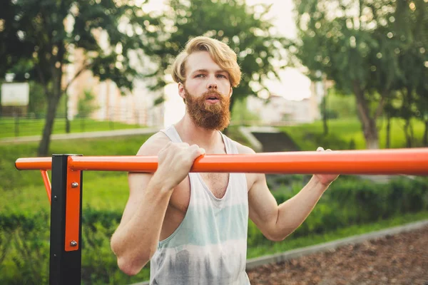 Portrait young bearded man standing on public sports ground and training on parallel bars. Handsome workout athlete. Portrait sporty man with beard, rest after training. Summer workout outdoors — Stock Photo, Image