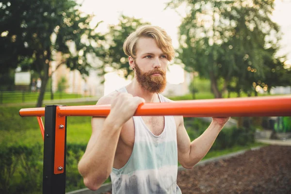 Portrait young bearded man standing on public sports ground and training on parallel bars. Handsome workout athlete. Portrait sporty man with beard, rest after training. Summer workout outdoors — Stock Photo, Image