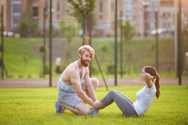 Sups fitness çift egzersiz çim dışında oturup. Çapraz eğitim de çalışan uygun insanlar. Kadın karın crunches eğitmen ile basın egzersiz yapıyor. Çift Yapıyor Sit-Ups Abdominal Crunch