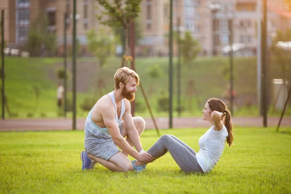 Sit up fitness coppia esercizio sedersi all'aperto in erba. Adatta alle persone che si allenano con il cross training. Donna che fa addominali crunches esercizio stampa con allenatore. Coppia che fa sit-up addominale Crunch — Foto Stock