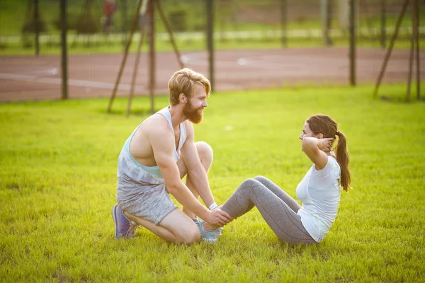 Sit ups fitness pareja ejercicio sentarse fuera en la hierba. Ajustar a las personas que trabajan a través de formación. Mujer haciendo abdominales ejercicios de prensa con entrenador. Pareja haciendo Sit-Ups Abdominal Crunch —  Fotos de Stock