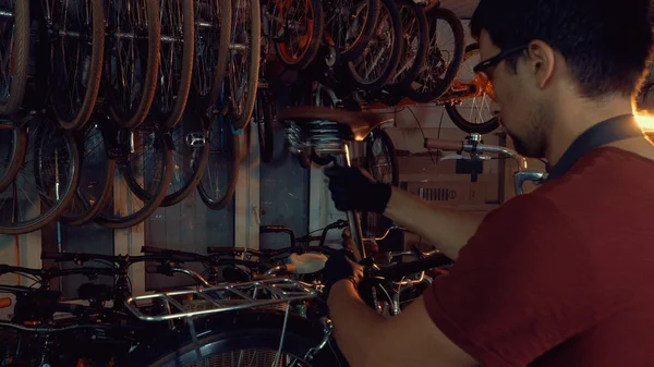 theme small business bike repair. A young Caucasian brunette man wearing safety goggles, gloves and an apron uses a hand tool to repair and adjust the bike in the workshop garage