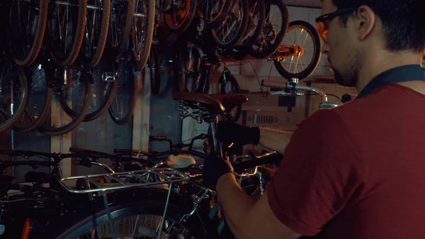 theme small business bike repair. A young Caucasian brunette man wearing safety goggles, gloves and an apron uses a hand tool to repair and adjust the bike in the workshop garage