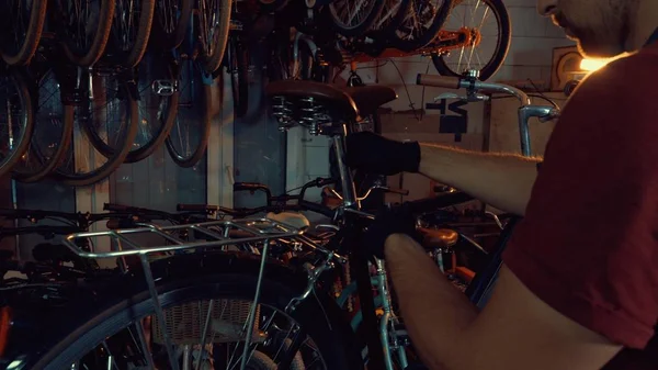 Naprawa rowerów tematu małych firm. Młoda brunetka kaukaski mężczyzna sobie bezpieczeństwa gogle, rękawice i fartuch używa narzędzia ręczne, naprawić i wyregulować rower w garażu warsztatu — Zdjęcie stockowe
