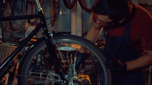 theme small business bike repair. Young brunette Caucasian man in protective glasses, gloves and fartuhe uses hand tools to repair and tuning Rim Brakes and wheel spinning bike in a garage workshop