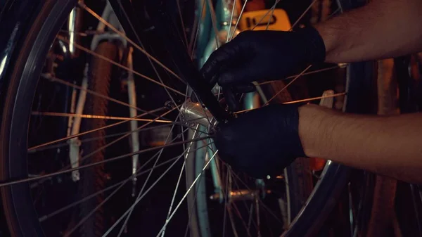 Tema små företag cykel reparation. En ung kaukasisk brunett man bär skyddsglasögon, handskar och ett förkläde använder en handverktyg för att reparera och installera cykelns Modguards i ett garage verkstad — Stockfoto