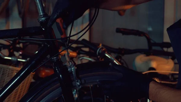 Тема малый бизнес ремонт велосипедов. Молодая брюнетка белый мужчина в защитных очках, перчатках и фартуке использует ручные инструменты для ремонта и настройки тормозов и крутящийся велосипед в гаражной мастерской — стоковое фото
