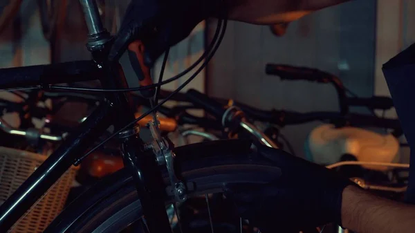 theme small business bike repair. Young brunette Caucasian man in protective glasses, gloves and fartuhe uses hand tools to repair and tuning Rim Brakes and wheel spinning bike in a garage workshop