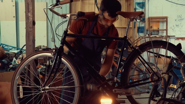 Thema Reparatur von Geschäftsfahrrädern. ein junger kaukasischer brünetter Mann mit Schutzbrille, Handschuhen und Schürze beharrt auf den Geschwindigkeitsschaltern am Fahrradlenker in der Werkstatt — Stockfoto