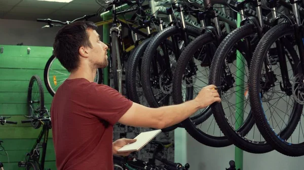 küçük iş bisiklet satış Tema. Genç beyaz erkek esmer küçük işletme sahibi, mağaza yöneticisi yapar notları, not defteri ve kalem Bisiklet mağazasında denetim listesi kullanır