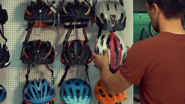 Genç bir beyaz adam baş koruma bölümü Bisiklet deposunda bir stand yakın duruyor. Küçük bir dükkanda bir bisiklet kask seçme