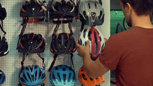 Genç bir beyaz adam baş koruma bölümü Bisiklet deposunda bir stand yakın duruyor. Küçük bir dükkanda bir bisiklet kask seçme