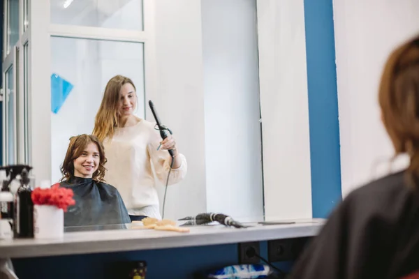 Schoonheid, kapsel concept, gelukkige jonge vrouw en kapper met strijkijzer maken kapsel in de kapsalon. Vrouw met haar gestileerde kapper. Verzacht Hair Curling. Stylist Gereedschap voor modellering gebruiken — Stockfoto