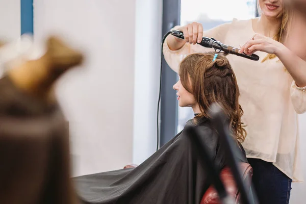 Beleza, conceito de penteado, mulher jovem feliz e cabeleireiro com ferro de cabelo fazendo penteado no salão de cabeleireiro. Mulher com cabelo cabeleireiro estilizado. Suaviza o encrespamento do cabelo. Stylist Usando Ferramenta para Modelagem — Fotografia de Stock