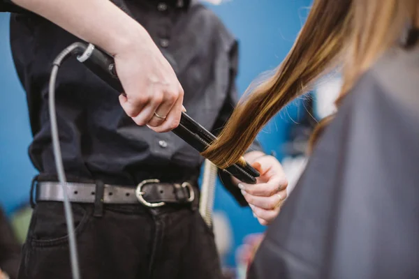 Skönhet, frisyr koncept, glad ung kvinna och frisör med hår järn gör frisyr på frisören. Kvinna med hår stiliserade frisör. Mjukar upp hårlockningen. Stylist Använda verktyg för modellering — Stockfoto