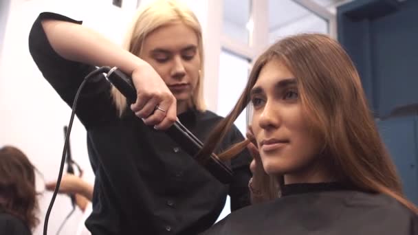 Piękno, koncepcja fryzury, szczęśliwa młoda kobieta i fryzjer z żelaza do włosów fryzurę w salonie fryzjerskim. Kobieta o włosy stylizowane fryzjer. Wygładza włosy curling. Stylista za pomocą narzędzia do modelowania — Wideo stockowe