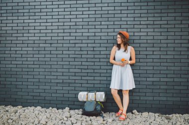 elbise tutan neşeli kız fincan götürmek. Hipster modeli şık yaz kıyafeti giyen Outdoors. sırt çantası olan kadın şehir caddesi boyunca yürüyor. tuğla duvarda hipster kız, modern genç yaşam tarzı