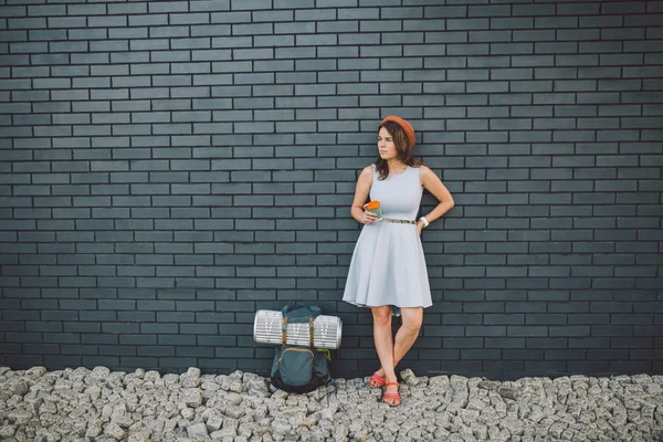 Chica alegre en vestido sosteniendo llevar taza. Hipster modelo con elegante traje de verano al aire libre. mujer con mochila pasea por la calle de la ciudad. chica hipster en la pared de ladrillo, estilo de vida de la adolescencia moderna — Foto de Stock