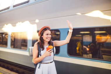 sırt çantası gezgin kadın tren istasyonu platformu yaz tatili seyahat kavramı el sallayarak. Kadın turist tebrik ve tren, seyahat kavramı zevk. Tema ulaşım ve seyahat