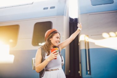 sırt çantası gezgin kadın tren istasyonu platformu yaz tatili seyahat kavramı el sallayarak. Kadın turist tebrik ve tren, seyahat kavramı zevk. Tema ulaşım ve seyahat