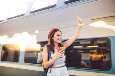 sırt çantası gezgin kadın tren istasyonu platformu yaz tatili seyahat kavramı el sallayarak. Kadın turist tebrik ve tren, seyahat kavramı zevk. Tema ulaşım ve seyahat