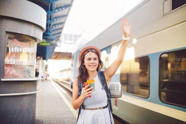 Mochila viajante mulher acenando mão na estação ferroviária plataforma verão férias viajando conceito. Feminino turista saudação e desfrutar no trem, conceito de viagem. Tema transporte e viagens — Fotografia de Stock