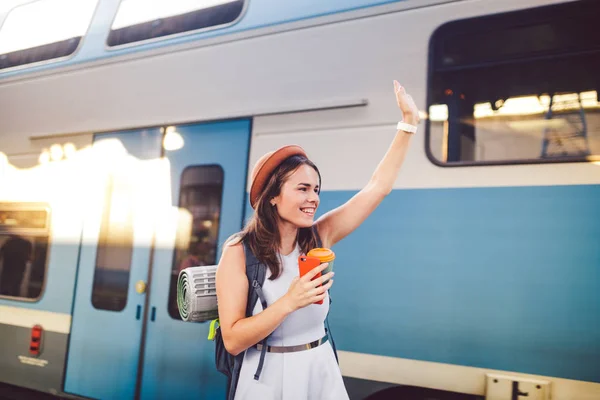 Рюкзак мандрівник жінка махає рукою на залізничній платформі літні канікули концепції подорожей. Жіночі туристичні вітання і насолоджуватися поїздом, концепцією подорожей. Тематика перевезення та подорожей — стокове фото