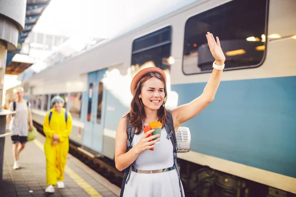 Mochila viajante mulher acenando mão na estação ferroviária plataforma verão férias viajando conceito. Feminino turista saudação e desfrutar no trem, conceito de viagem. Tema transporte e viagens — Fotografia de Stock