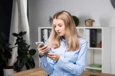 Ofiste duran cep telefonu ile iş kadını portresi. ofiste cep telefonu tutan genç Kafkas iş kadını. telefon kullanan iş kadını. İş kadını akıllı telefon ile mesaj gönderiyor