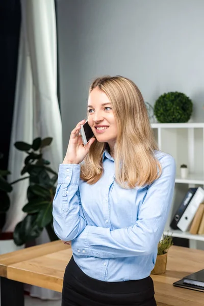 Retrato de mulher de negócios com telefone celular em pé no escritório. jovem mulher de negócios caucasiana segurando telefone celular no escritório. mulher de negócios usando telefone. Executivo de negócios conversando no celular — Fotografia de Stock