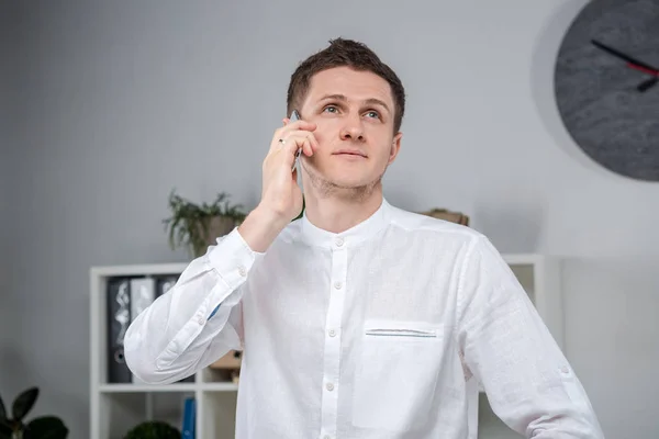 Atractivo joven hombre de negocios usando un teléfono celular. Hombre de negocios alegre con Smartphone de pie en una oficina. Retrato del hombre en la oficina con teléfono. Empresario usando teléfono en el lugar de trabajo en la oficina — Foto de Stock