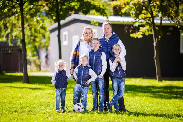 Gelukkige familie buitenshuis. Gelukkige blanke familie die buiten hun huis staat en knuffelen. Gezin met vier kinderen in voor huis. Grote gelukkige familie staat naast hun huis glimlachend en uitziende camera — Stockfoto