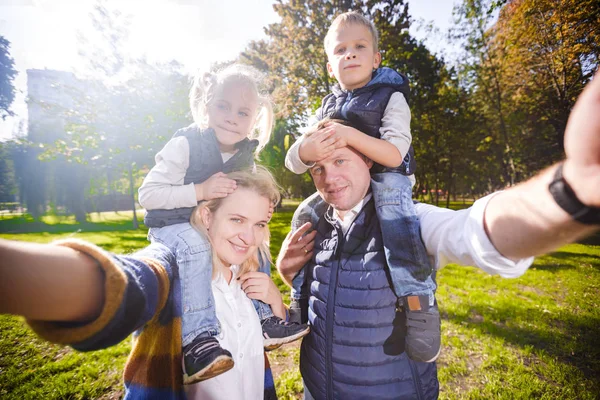 Selfie fotoğrafı çeken genç çift, omuzlarında oğlu ve kızını taşıyan selfie fotoğrafı yla mutlu bir gülümseme pozu veriyor. Point View Shot Baba, anne Çocuklar Selfie için poz. birlikte zevk aile — Stok fotoğraf