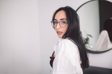 Erkek gömlek moda lüks bayan. Aynanın yanındaki yatak odasında poz veren iç çamaşırı ve gömlekli güzellik kadını. Iç çamaşırı baştan çıkarıcı seksi kız modeli Trendy portre. Iç Çamaşırı Poz Seksi Genç Kadın