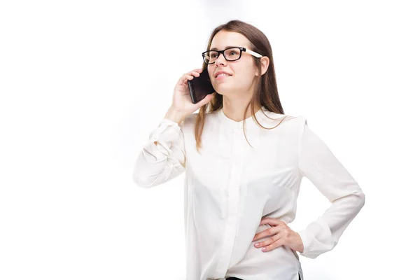 Mulher de negócios sorridente com óculos a falar no telemóvel. Menina bonita em camisa branca no fundo isolado branco falando no telefone móvel. Mulher de camisa com telemóvel. Espaço para cópia. Em branco — Fotografia de Stock