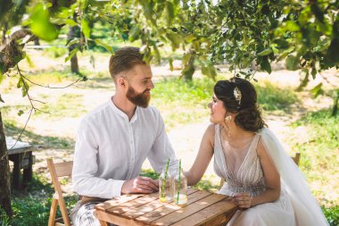 Çekici çift yeni evliler, mutlu ve neşeli an. gelin ve damat ormanda iki için belirlenen masada oturup. Kavram romantik tarih. Düğün çift kafe masada oturan ve sevgiyle birbirlerine bakmak