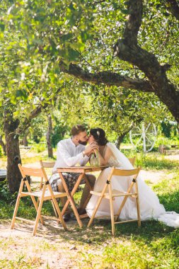 Çekici çift yeni evliler, mutlu ve neşeli an. gelin ve damat ormanda iki için belirlenen masada oturup. Kavram romantik tarih. Düğün çift kafe masada oturan ve sevgiyle birbirlerine bakmak