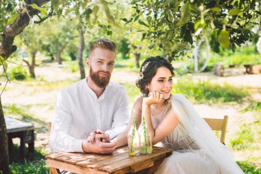 Çekici çift yeni evliler, mutlu ve neşeli an. gelin ve damat ormanda iki için belirlenen masada oturup. Kavram romantik tarih. Düğün çift kafe masada oturan ve sevgiyle birbirlerine bakmak
