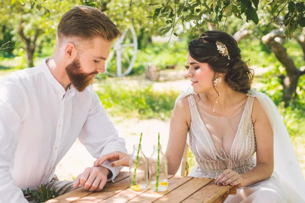 Çekici çift yeni evliler, mutlu ve neşeli an. gelin ve damat ormanda iki için belirlenen masada oturup. Kavram romantik tarih. Düğün çift kafe masada oturan ve sevgiyle birbirlerine bakmak