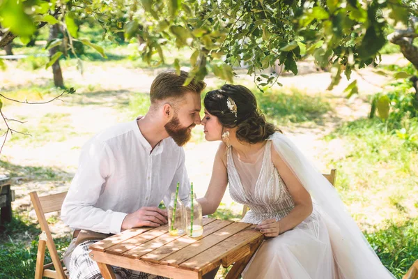 Casal atraente recém-casados, momento feliz e alegre. noiva e noivo sentam-se à mesa para dois na floresta. Conceito encontro romântico. Casamento casal sentado na mesa de café e amorosamente olhar um para o outro — Fotografia de Stock