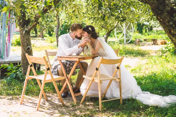 Casal atraente recém-casados, momento feliz e alegre. noiva e noivo sentam-se à mesa para dois na floresta. Conceito encontro romântico. Casamento casal sentado na mesa de café e amorosamente olhar um para o outro — Fotografia de Stock