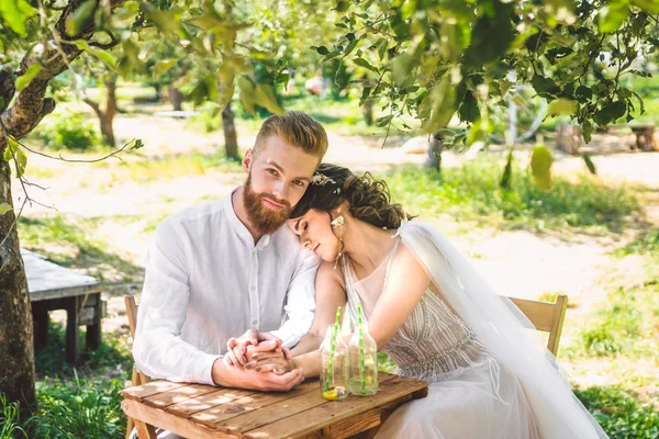 Çekici çift yeni evliler, mutlu ve neşeli an. gelin ve damat ormanda iki için belirlenen masada oturup. Kavram romantik tarih. Düğün çift kafe masada oturan ve sevgiyle birbirlerine bakmak